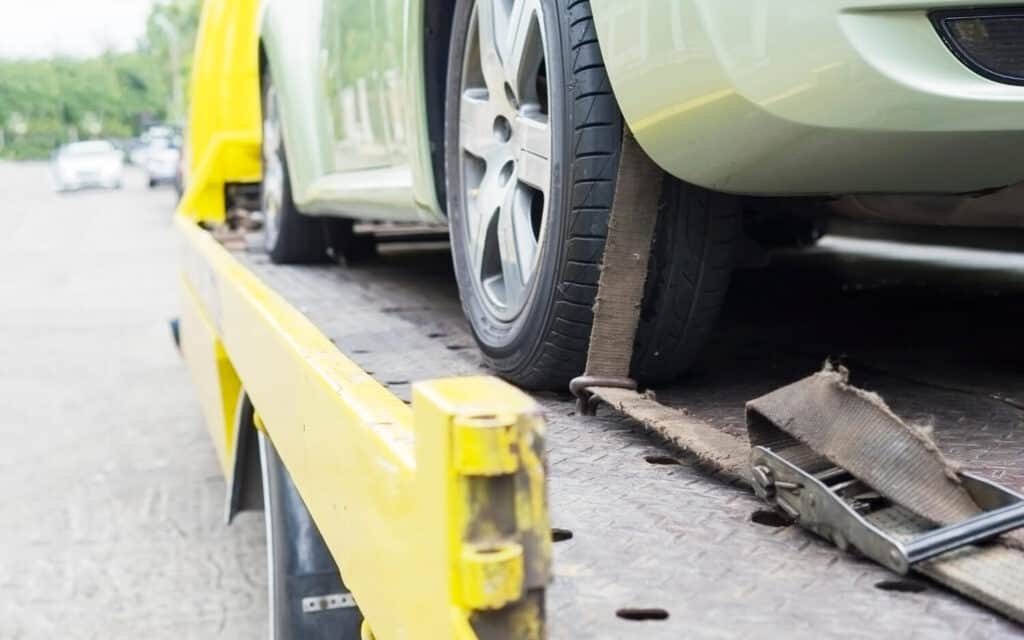 Zbliżenie na samochód zabezpieczony z tyłu żółtą lawetą z paskiem wokół przedniej opony, gotowy do transportu i profesjonalnej pomocy drogowej.