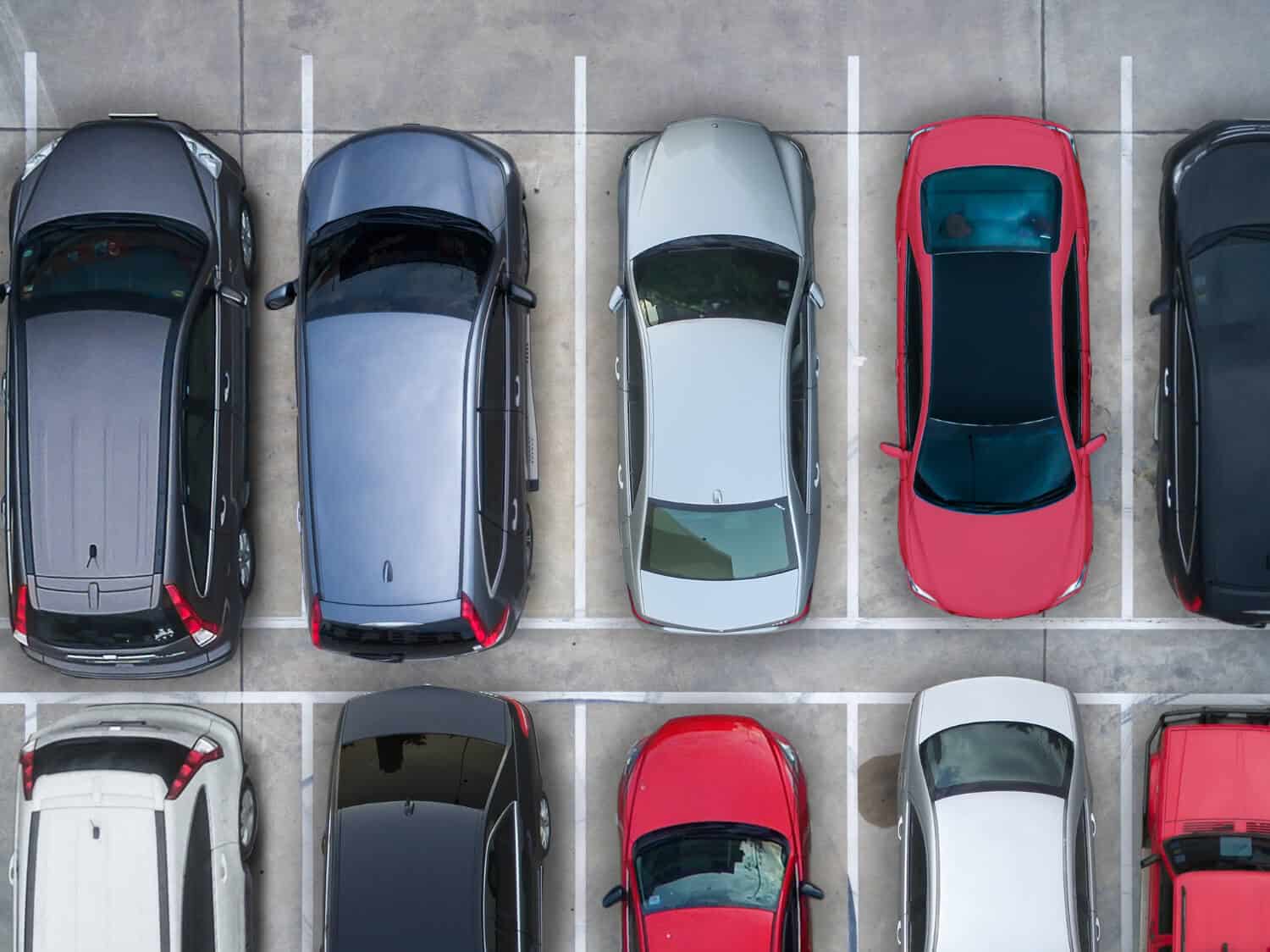 Widok z lotu ptaka na kilka samochodów zaparkowanych obok siebie na parkingu, z mieszanką kolorów, a także lawetą do holowania i pomocy drogowej, wszystkie oddzielone białymi liniami parkingowymi na betonowej powierzchni.