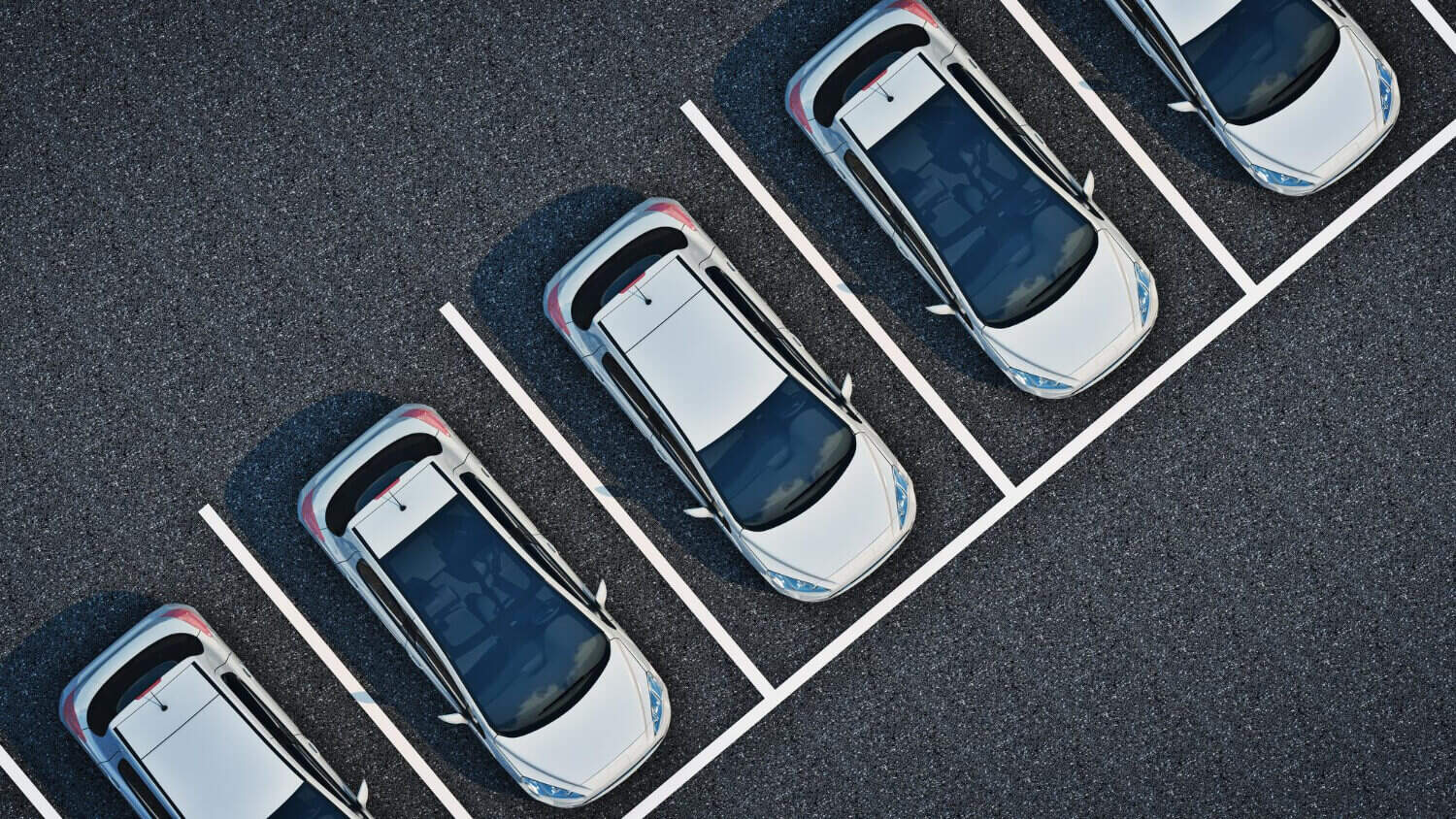 Widok z lotu ptaka na pięć srebrnych samochodów zaparkowanych po przekątnej w oznaczonych miejscach na asfaltowym parkingu, idealnie ustawionych w rzędzie - idealne dla lawety lub szybkiej pomocy drogowej w razie potrzeby.